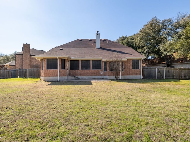 back of house featuring brick siding, a lawn, a chimney, and a fenced backyard