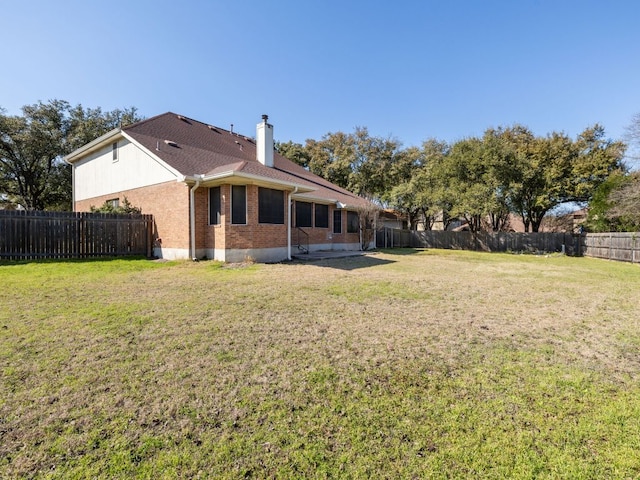 rear view of property featuring a yard, a fenced backyard, a chimney, and brick siding