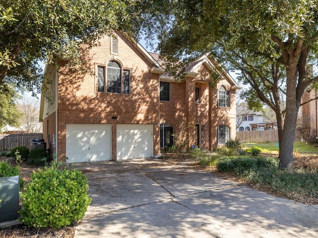 traditional-style home with a garage, concrete driveway, brick siding, and fence