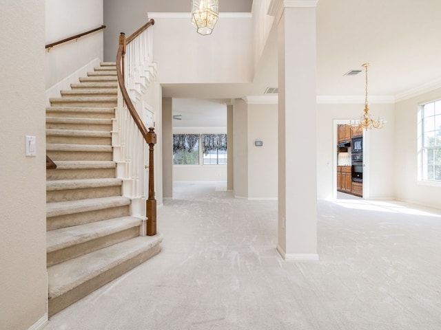 carpeted entryway featuring crown molding, stairs, visible vents, and a notable chandelier