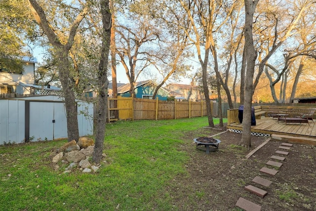 view of yard with an outdoor fire pit, a fenced backyard, an outbuilding, a storage unit, and a deck