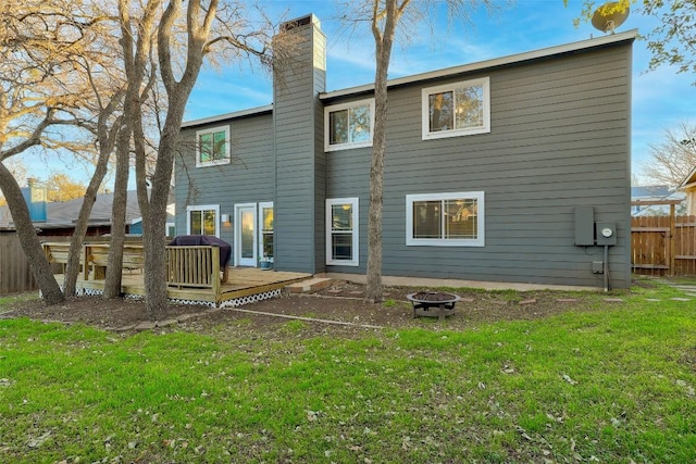 rear view of property featuring a yard, a chimney, fence, a deck, and a fire pit