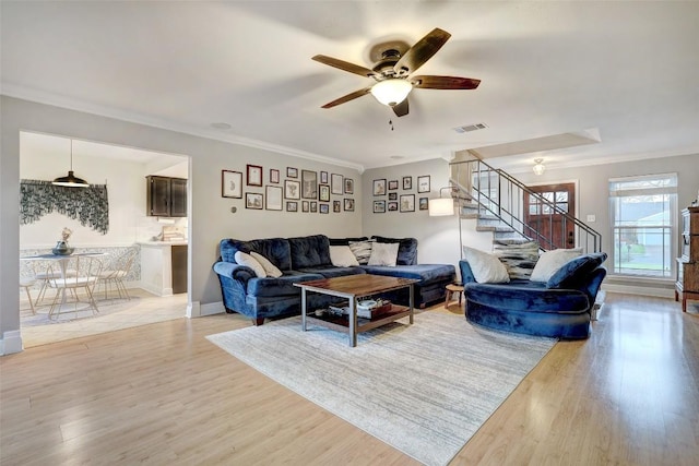 living room featuring visible vents, baseboards, stairway, light wood finished floors, and crown molding