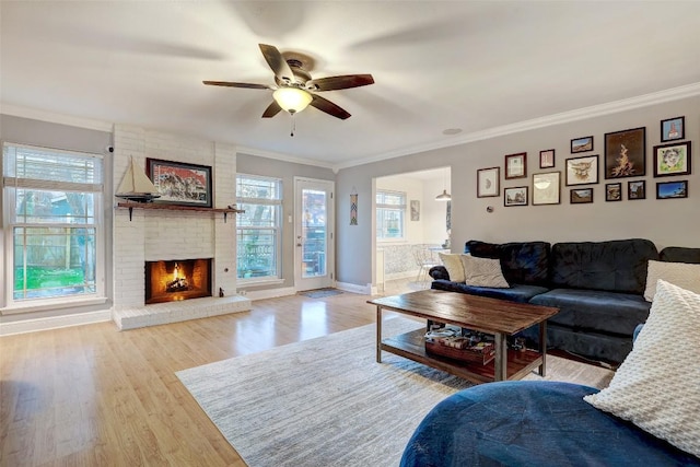 living room with baseboards, ceiling fan, wood finished floors, crown molding, and a brick fireplace