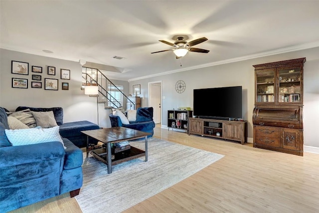 living room with light wood finished floors, visible vents, stairway, ornamental molding, and ceiling fan