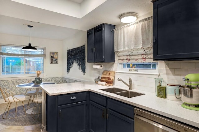 kitchen featuring a peninsula, stainless steel dishwasher, light countertops, and a sink