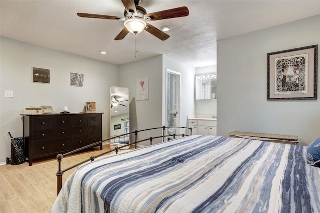 bedroom with a textured ceiling, ceiling fan, connected bathroom, light wood-style flooring, and baseboards