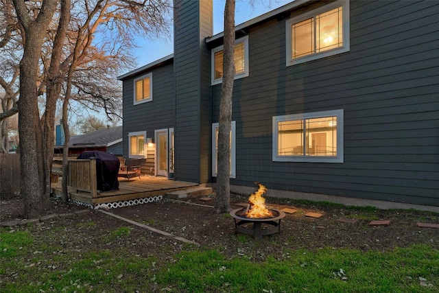 rear view of house with an outdoor fire pit, a chimney, and a deck