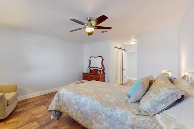 bedroom with visible vents, a ceiling fan, wood finished floors, a barn door, and baseboards