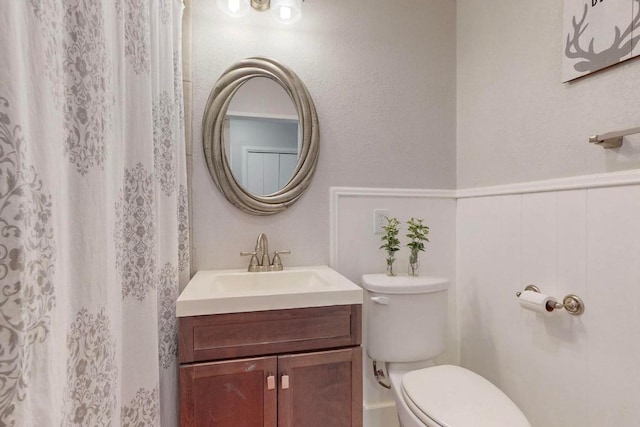 bathroom featuring a wainscoted wall, toilet, and vanity