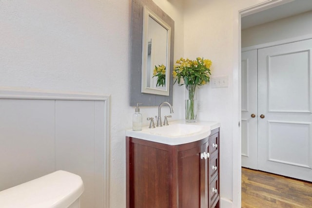 half bath with vanity, toilet, and wood finished floors