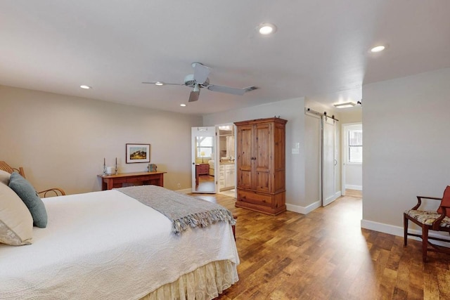 bedroom with a barn door, recessed lighting, wood finished floors, and baseboards