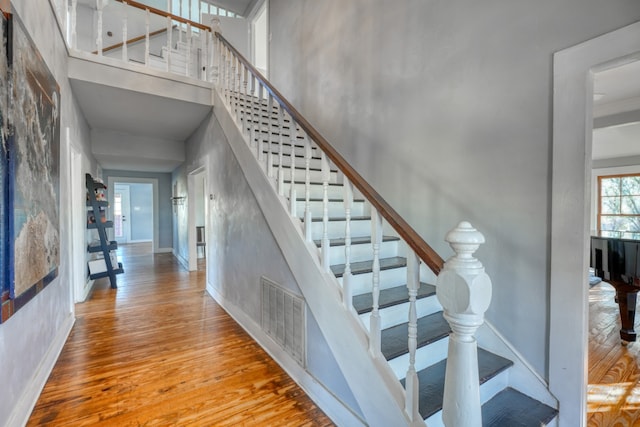 stairs featuring baseboards, a high ceiling, visible vents, and wood finished floors