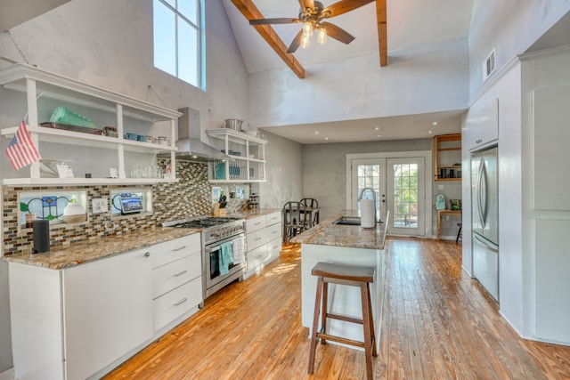 kitchen with open shelves, white cabinets, a sink, wall chimney range hood, and high end stove