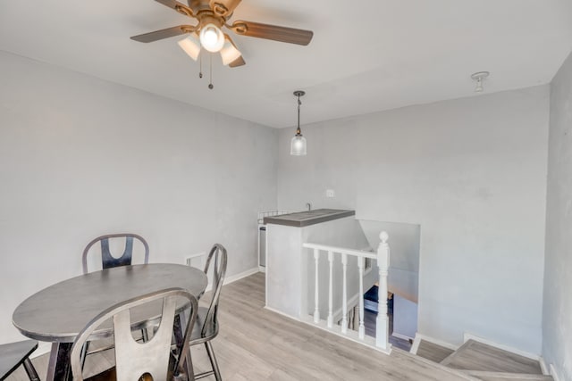 dining space with a ceiling fan, baseboards, and light wood finished floors