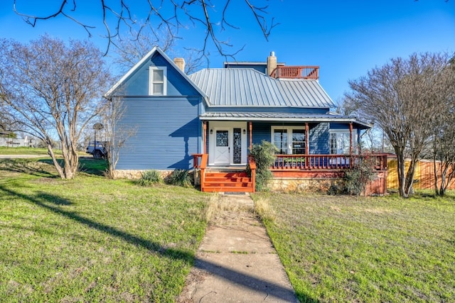 view of front of property with a front yard, covered porch, metal roof, and a chimney