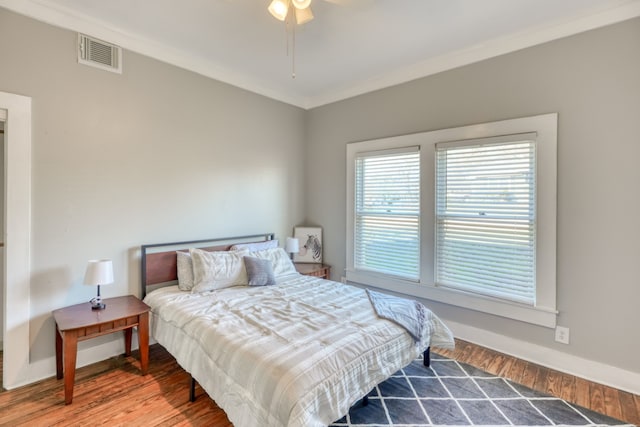 bedroom featuring visible vents, ornamental molding, a ceiling fan, wood finished floors, and baseboards