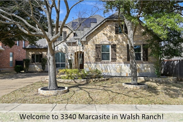 view of front of house with stone siding, fence, solar panels, and concrete driveway