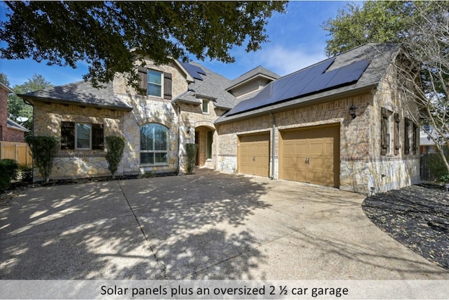 french country home with an attached garage, stone siding, driveway, and solar panels