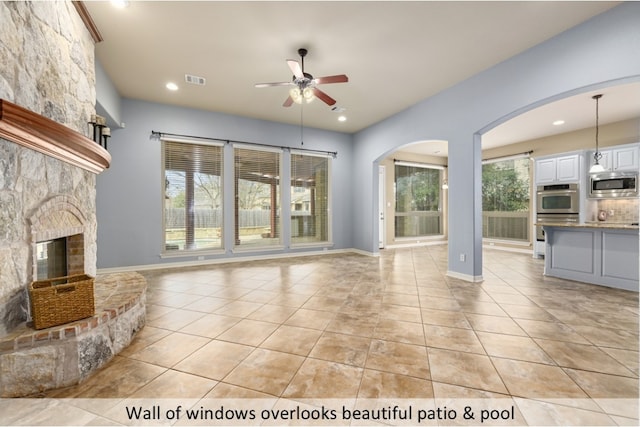 unfurnished living room with visible vents, baseboards, ceiling fan, a stone fireplace, and light tile patterned flooring