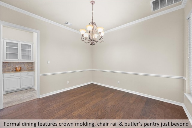 empty room with crown molding, visible vents, baseboards, wood finished floors, and a notable chandelier