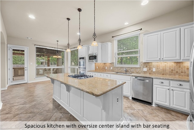kitchen featuring white cabinets, a sink, appliances with stainless steel finishes, a center island, and backsplash