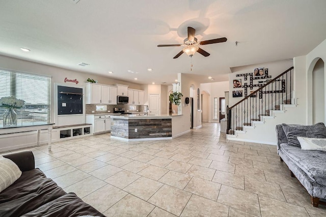 living room with stairway, light tile patterned floors, a ceiling fan, and arched walkways