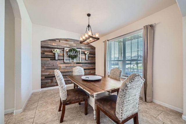 dining room featuring wooden walls, an accent wall, a chandelier, light tile patterned floors, and arched walkways