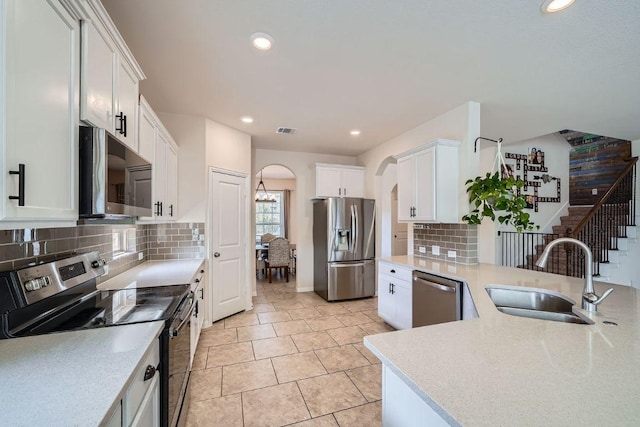 kitchen featuring a sink, stainless steel appliances, arched walkways, white cabinets, and light countertops