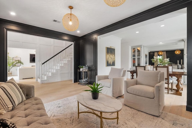 living area featuring visible vents, crown molding, stairway, light wood-style floors, and a decorative wall