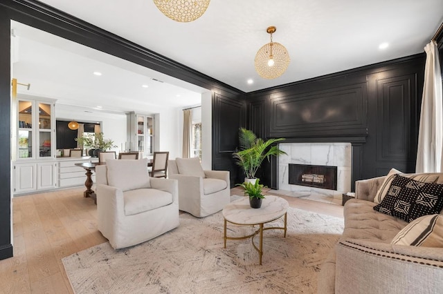 living room with recessed lighting, ornamental molding, light wood-style floors, and a premium fireplace