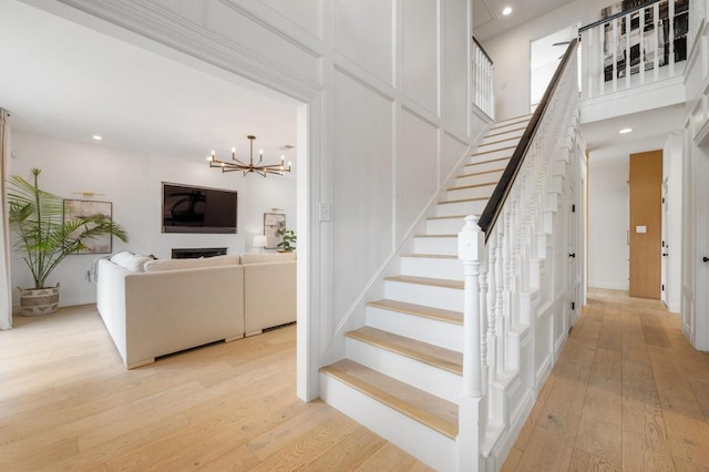 stairway featuring a high ceiling, an inviting chandelier, hardwood / wood-style floors, and a fireplace