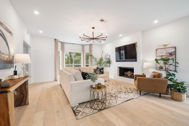 living room with visible vents, recessed lighting, a lit fireplace, light wood-type flooring, and a chandelier