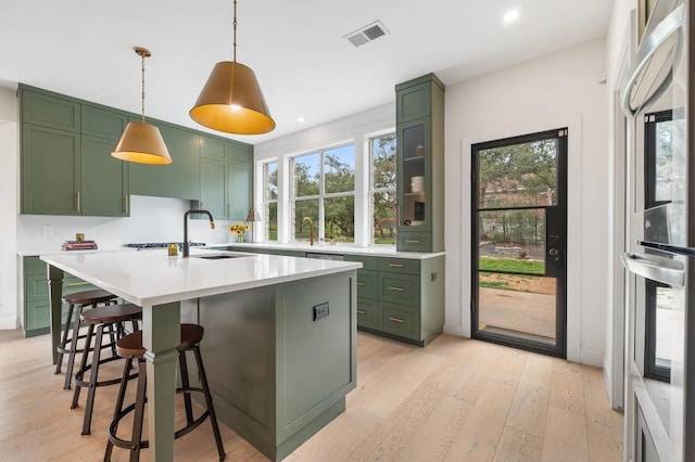 kitchen with green cabinetry, light countertops, a kitchen breakfast bar, light wood-style floors, and a sink