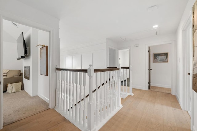 hallway with an upstairs landing, light wood finished floors, attic access, and baseboards