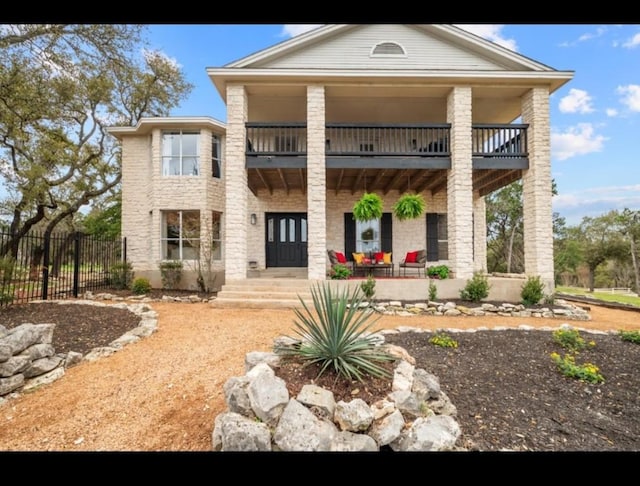 neoclassical home with covered porch, a balcony, and fence