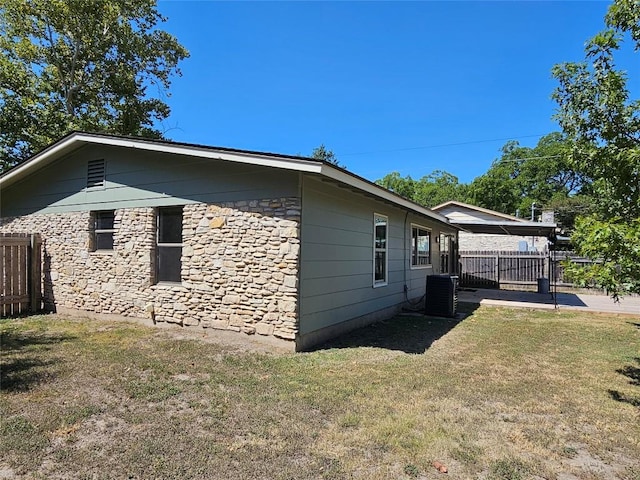 view of property exterior with stone siding, a yard, fence, and central AC unit