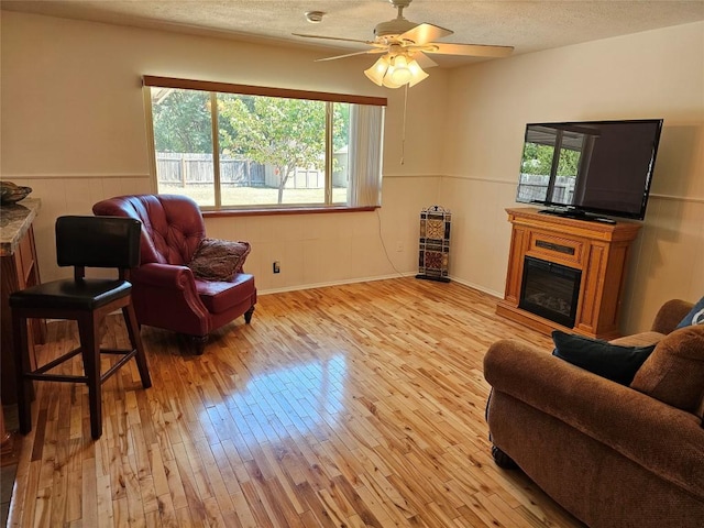 living room with hardwood / wood-style flooring, wainscoting, a textured ceiling, and a glass covered fireplace