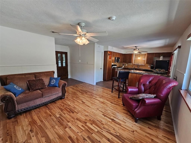 living room with a ceiling fan, light wood-type flooring, a wainscoted wall, and a textured ceiling