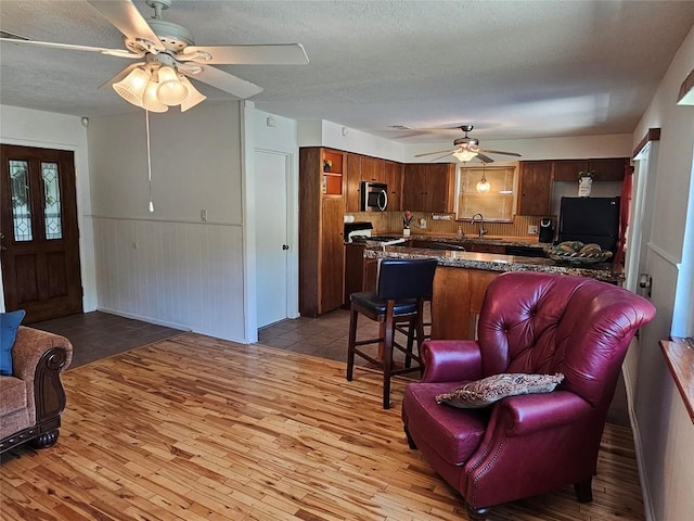 living room featuring light wood-style floors, wainscoting, a textured ceiling, and a ceiling fan