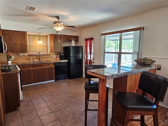 kitchen with visible vents, wainscoting, a breakfast bar, black appliances, and a sink