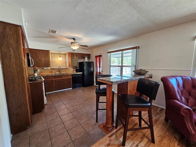 kitchen with a wainscoted wall, visible vents, open floor plan, a sink, and black appliances