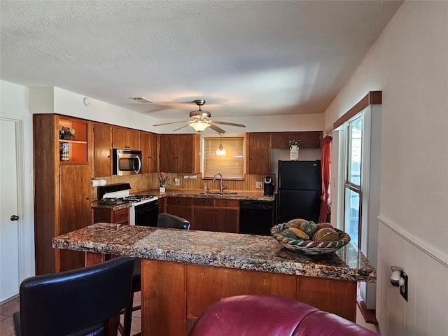 kitchen featuring brown cabinets, a wainscoted wall, a sink, a textured ceiling, and black appliances