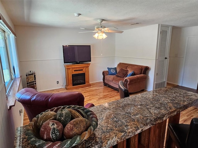 living room with a fireplace, visible vents, a ceiling fan, a textured ceiling, and light wood-type flooring