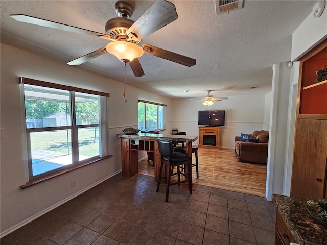 dining room featuring a fireplace, visible vents, a ceiling fan, a textured ceiling, and dark tile patterned flooring