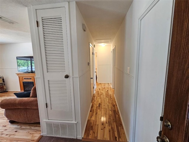 hall with light wood-style flooring, attic access, visible vents, and baseboards