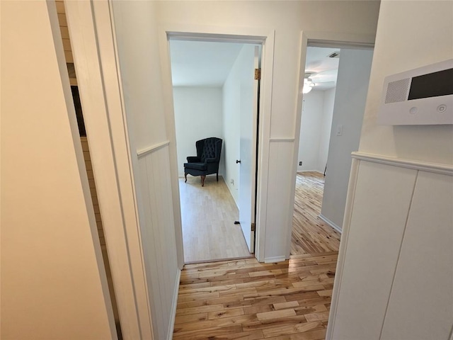 corridor with a wainscoted wall and wood finished floors