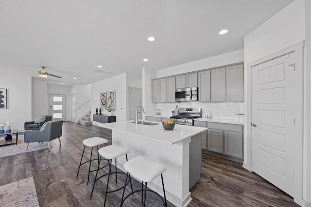 10410 Fulton Ave, Austin, TX 78754 - kitchen with stainless steel appliances, gray cabinetry, a sink, dark wood-style floors, and a kitchen breakfast bar