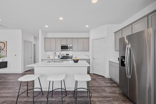 10410 Fulton Ave, Austin, TX 78754 - kitchen featuring stainless steel appliances, gray cabinets, a sink, an island with sink, and a breakfast bar area