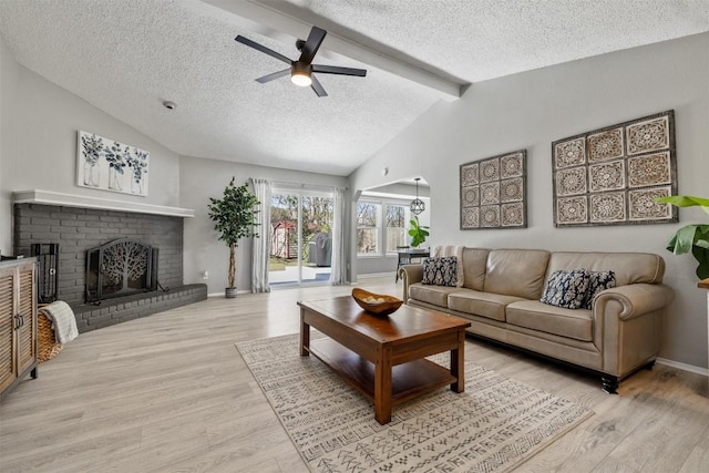 living room with a ceiling fan, lofted ceiling with beams, a textured ceiling, light wood-type flooring, and a brick fireplace